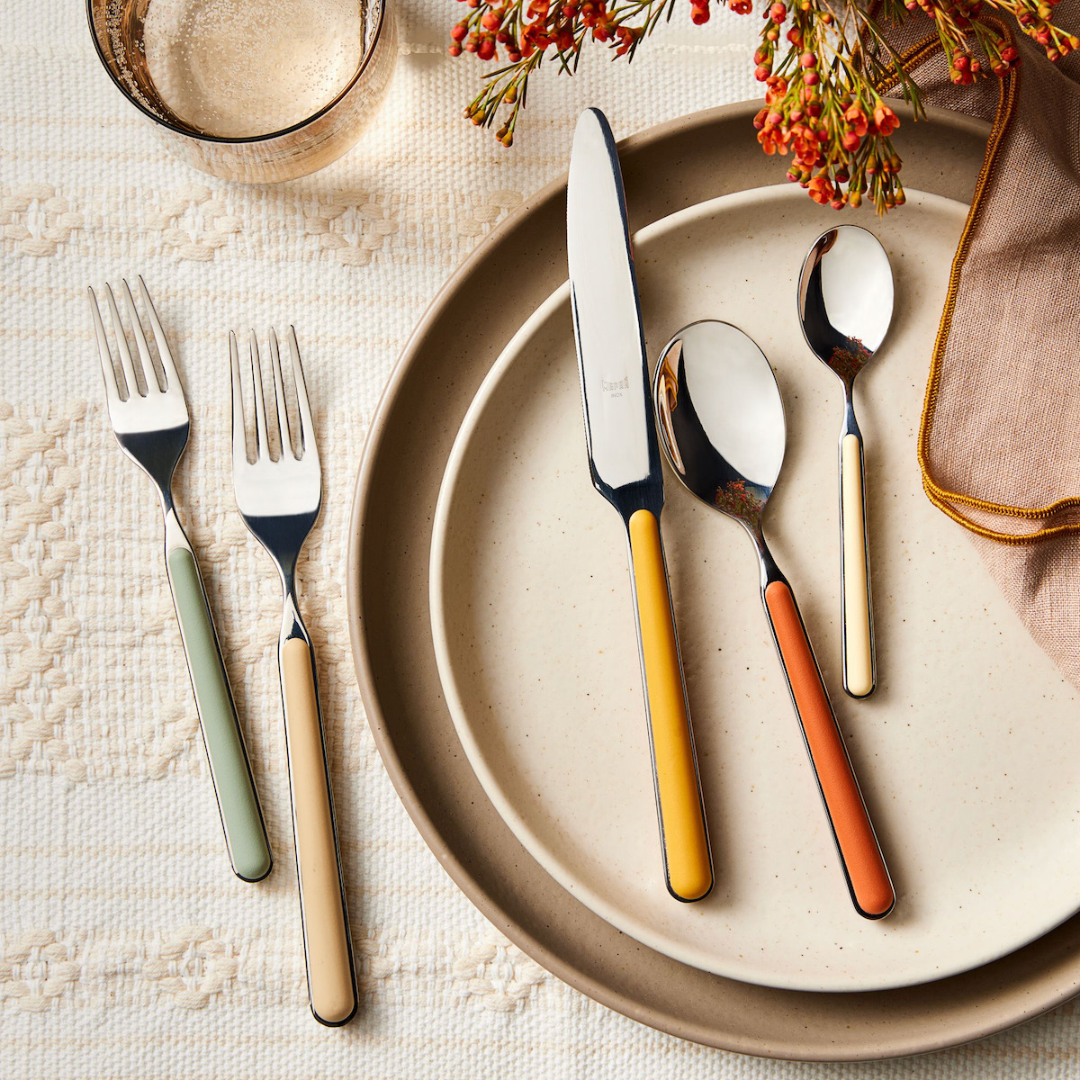 Two forks, a knife, and two spoons with multicolored handles staged over a ceramic ware plate 