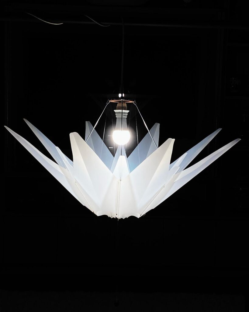 A geometric white lamp shade sits below a lightbulb against a black background.