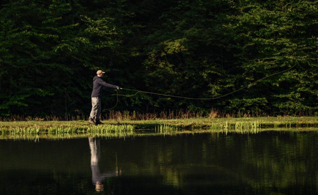 A man casts a fishing pole at the side of a lake.