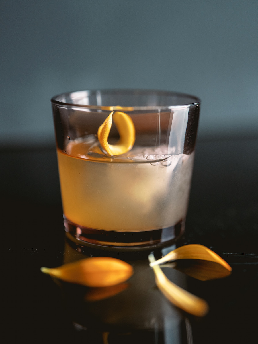 A mezcal cocktail on a black background, garnished with an orange slice