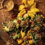 On a table sets various heads of grilled sunflowers with a bacon vinaigrette in a cup up in the top left corner.