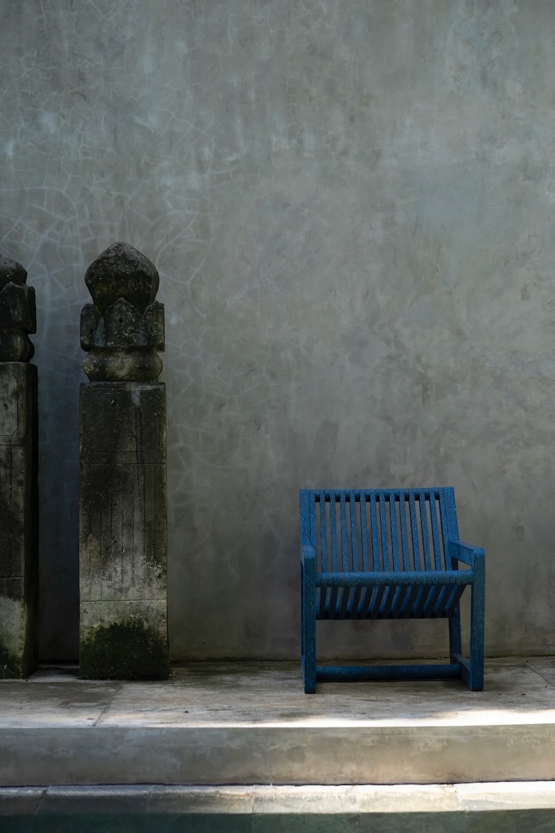 A dark blue lounge chair sits against a grey concrete walll.