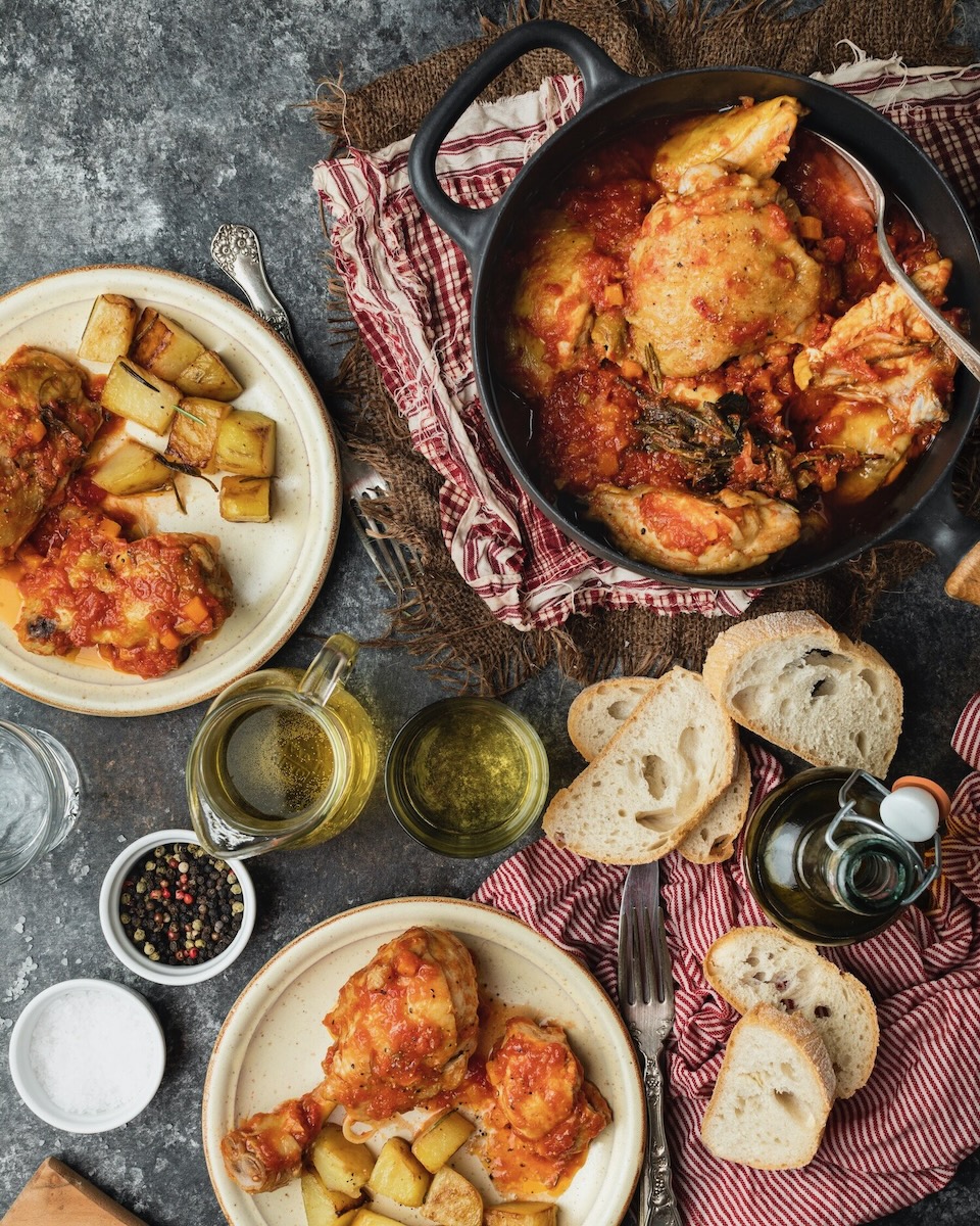 Various dishes on a dark grey countertop show chicken and potatoes in large groups.