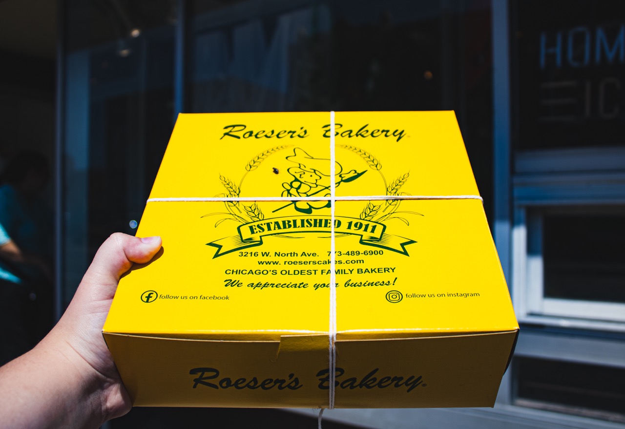 A yellow pastry box from Roeser's Bakery is held outside of the bakery. 