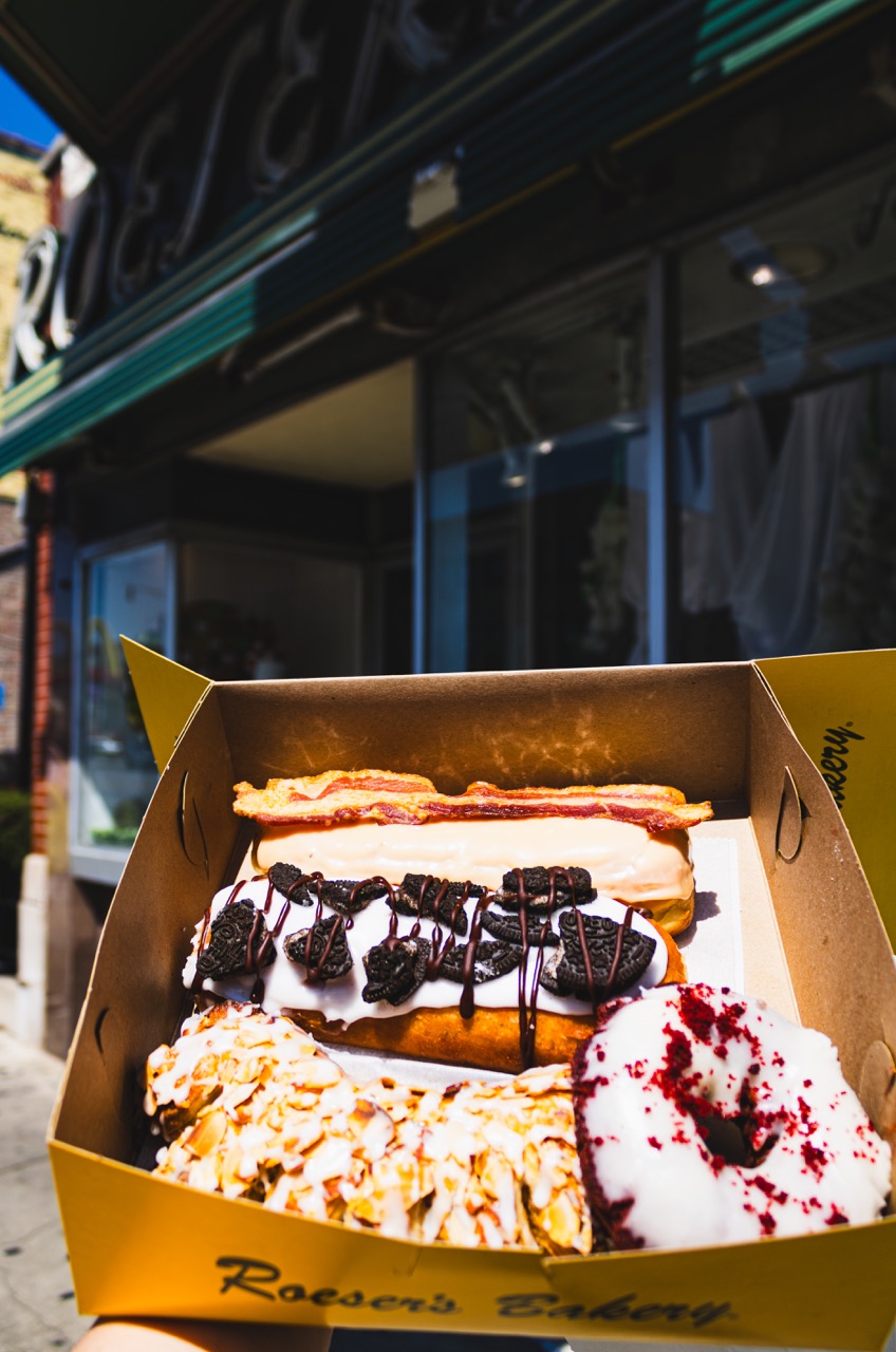 A box of 3 donuts and one bear claw is held outside of Roeser's bakery.