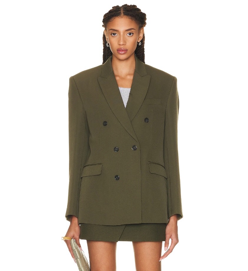 A woman stands in a boxy green blazer as a part of fall fashion trends. 