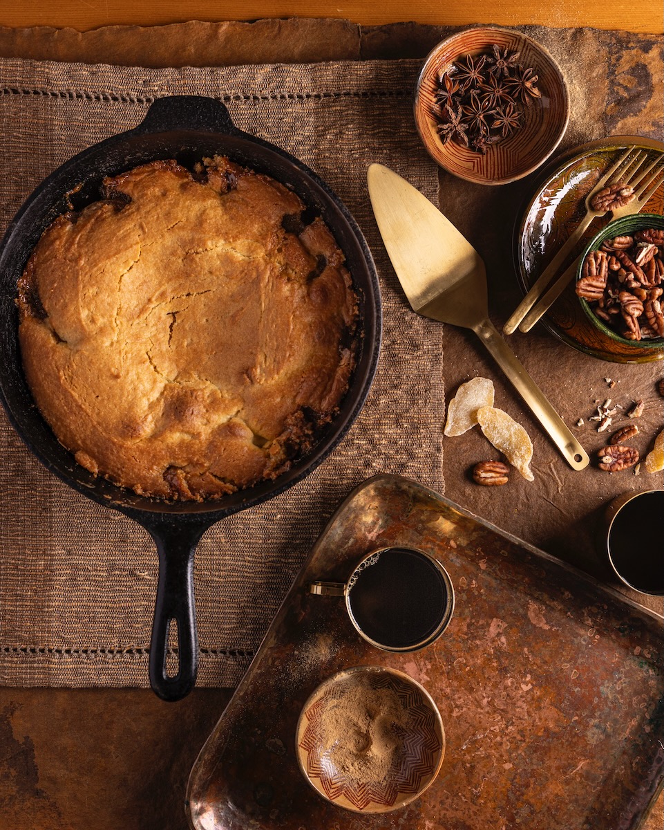 A pear upside down cake sits in a cast iron pan on a wooden table with a pie spatula nearby. 