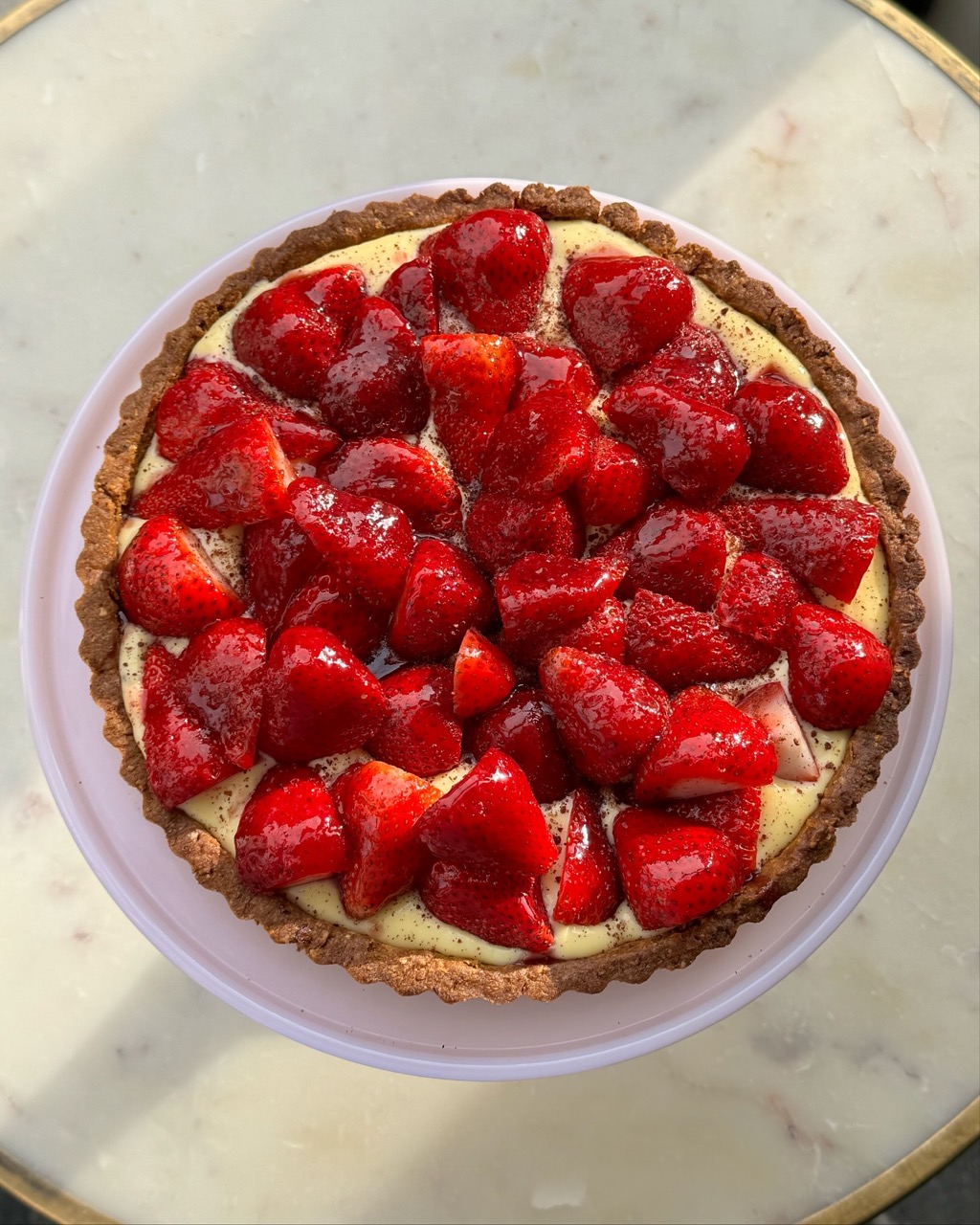 A strawberry tart sits in a round pan on top of a white table.