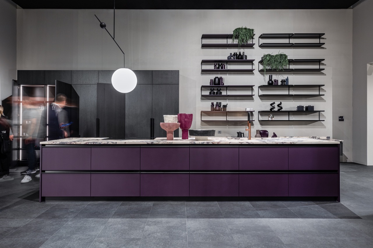 A long purple counter with a marble white top is in a kitchen with a round light hanging above it. 