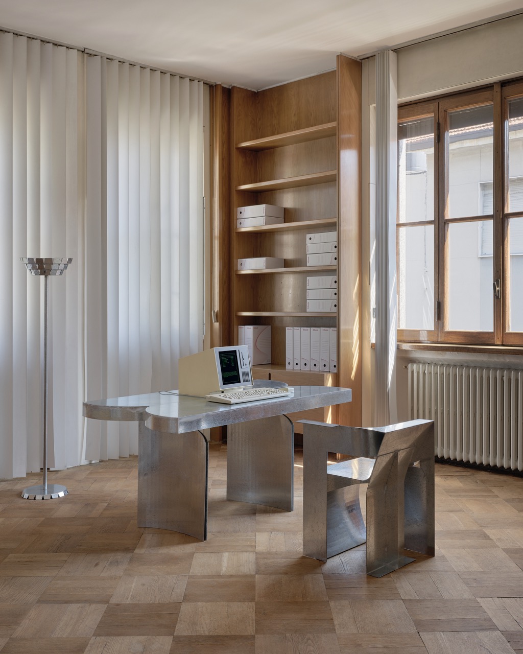 An aluminum desk sits beside an aluminum chair in an open office space.