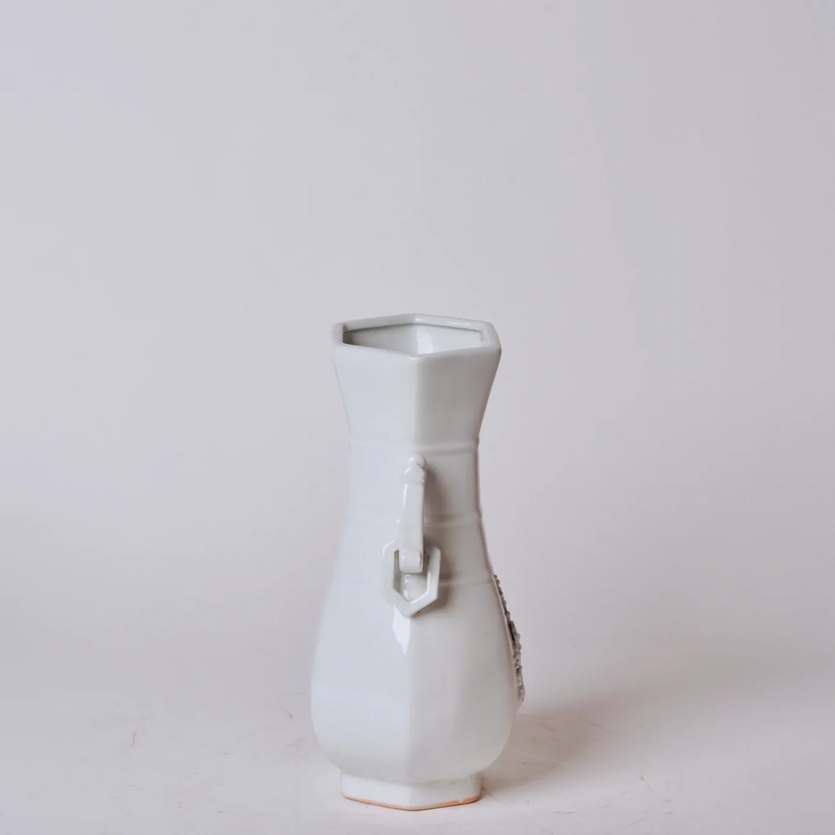 A white porcelain vase with a small dragon insignia on it on a white background