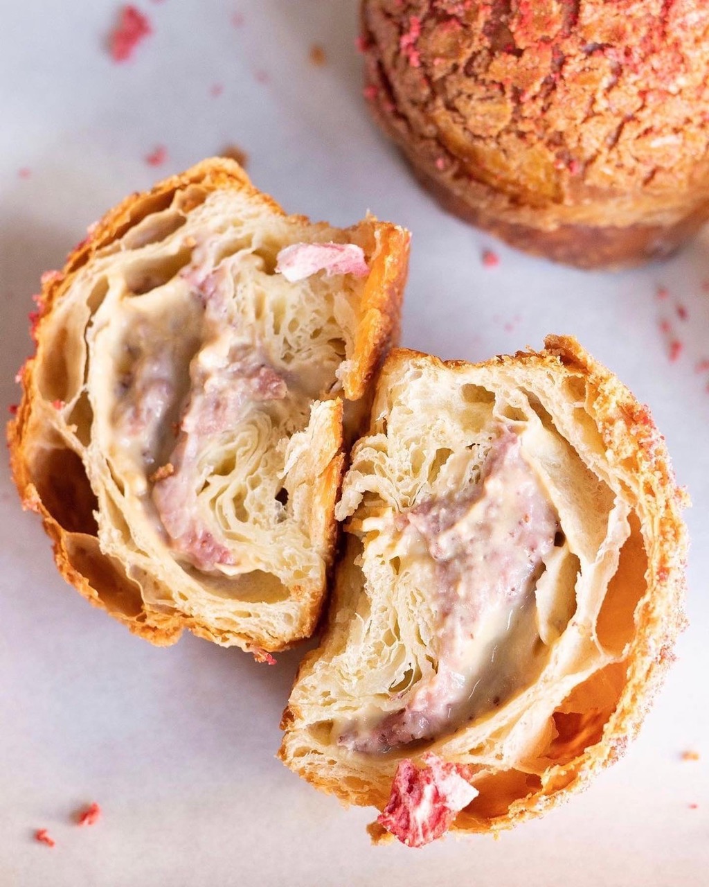 A baked bun from Win Son bakery in NYC is broken open with pink specks throughout on a white table.