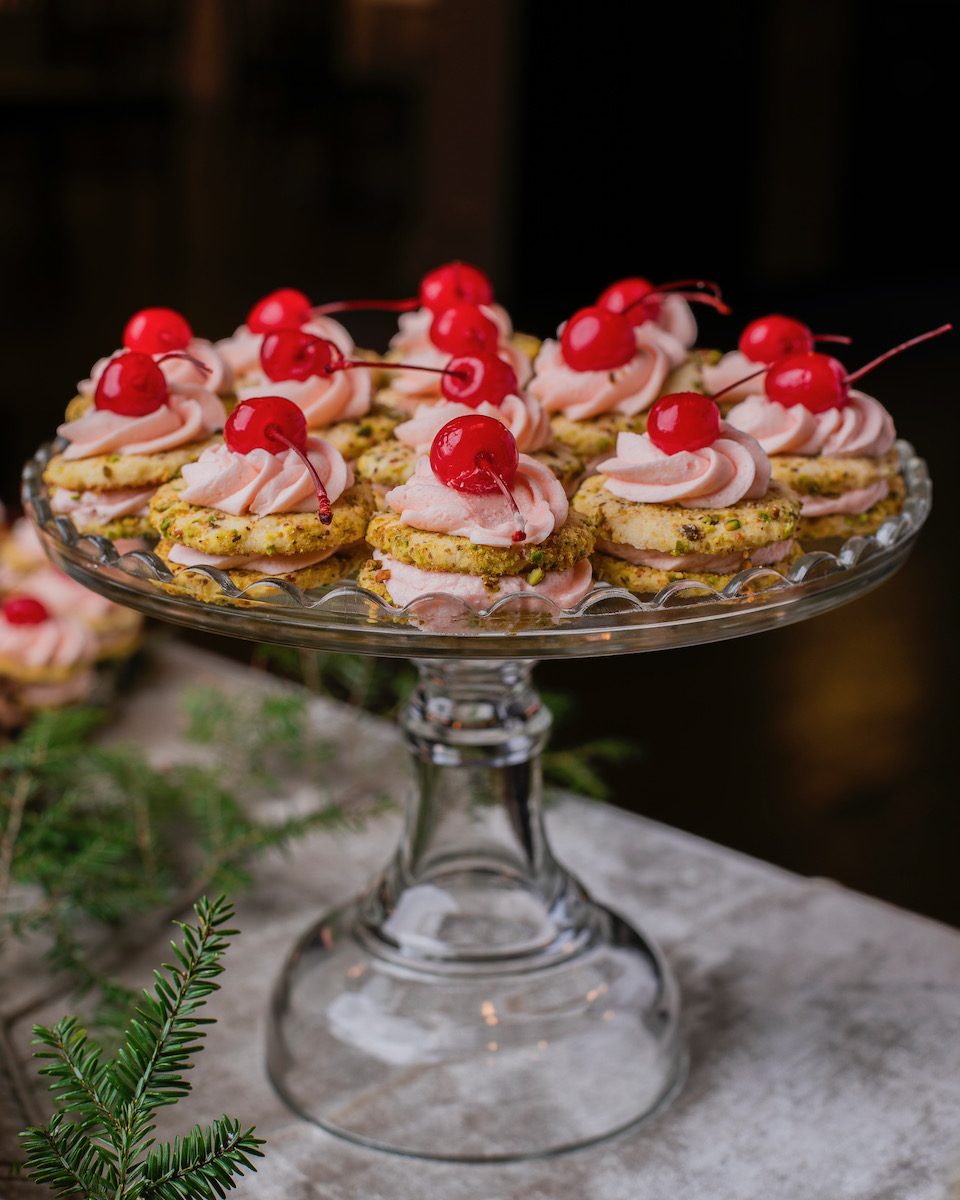 A glass plate of cherry pistachio sandwich cookies 