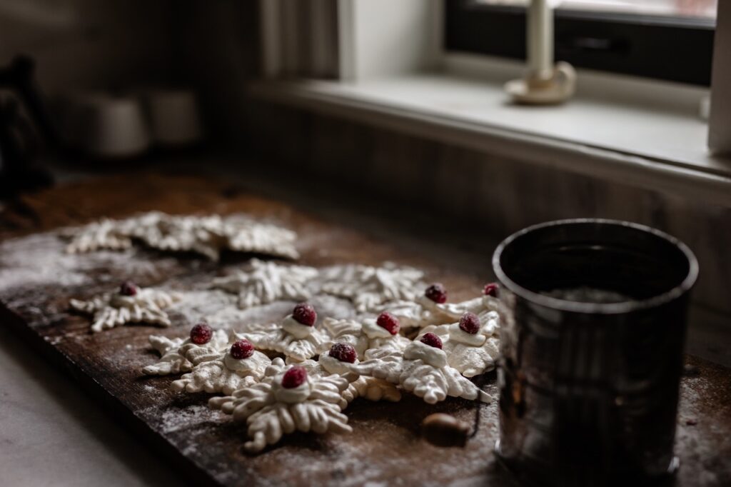 Snowflake meringue cookies with cherries on top sit in front of a window and beside a cup of tea.