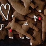 A pile of gingerbread cookies decorated with white icing and red bulb sprinles.