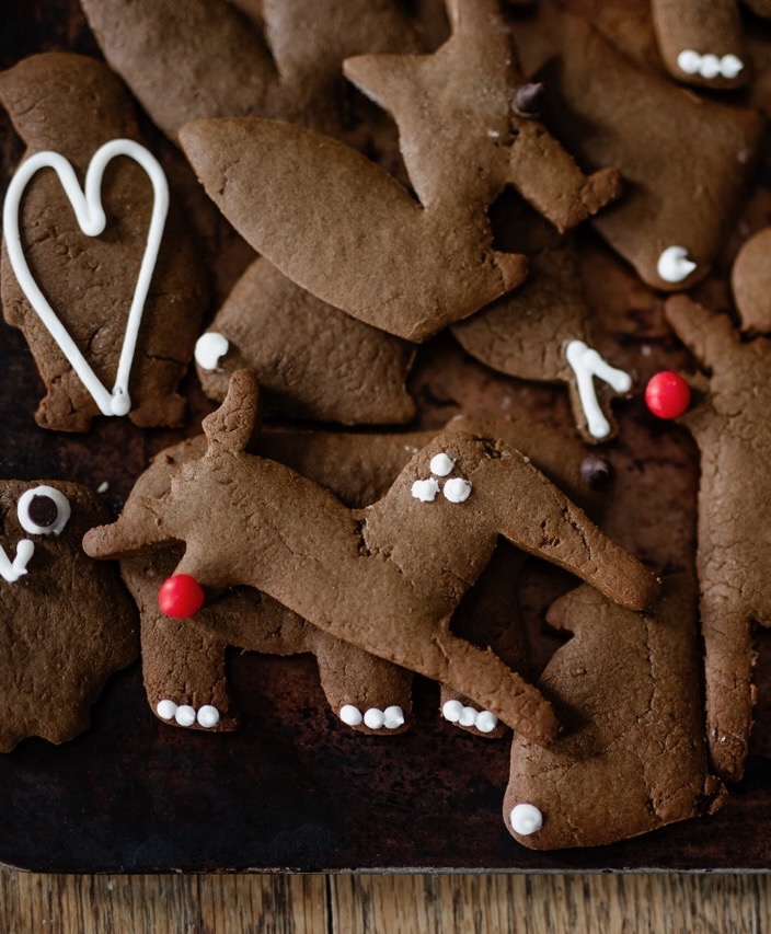 A pile of gingerbread cookies decorated with white icing and red bulb sprinles.