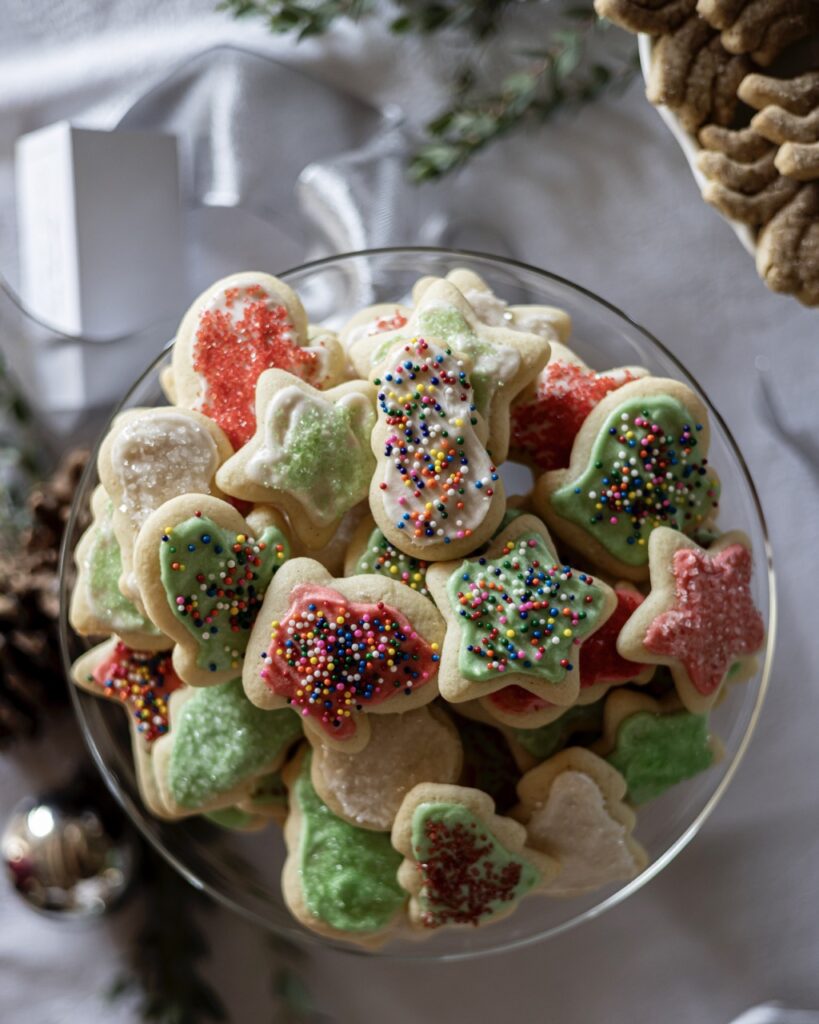 A bowl full of Iced Sugar Cookies in green and red colors and various shapes like stars, mittens, and snowmen.