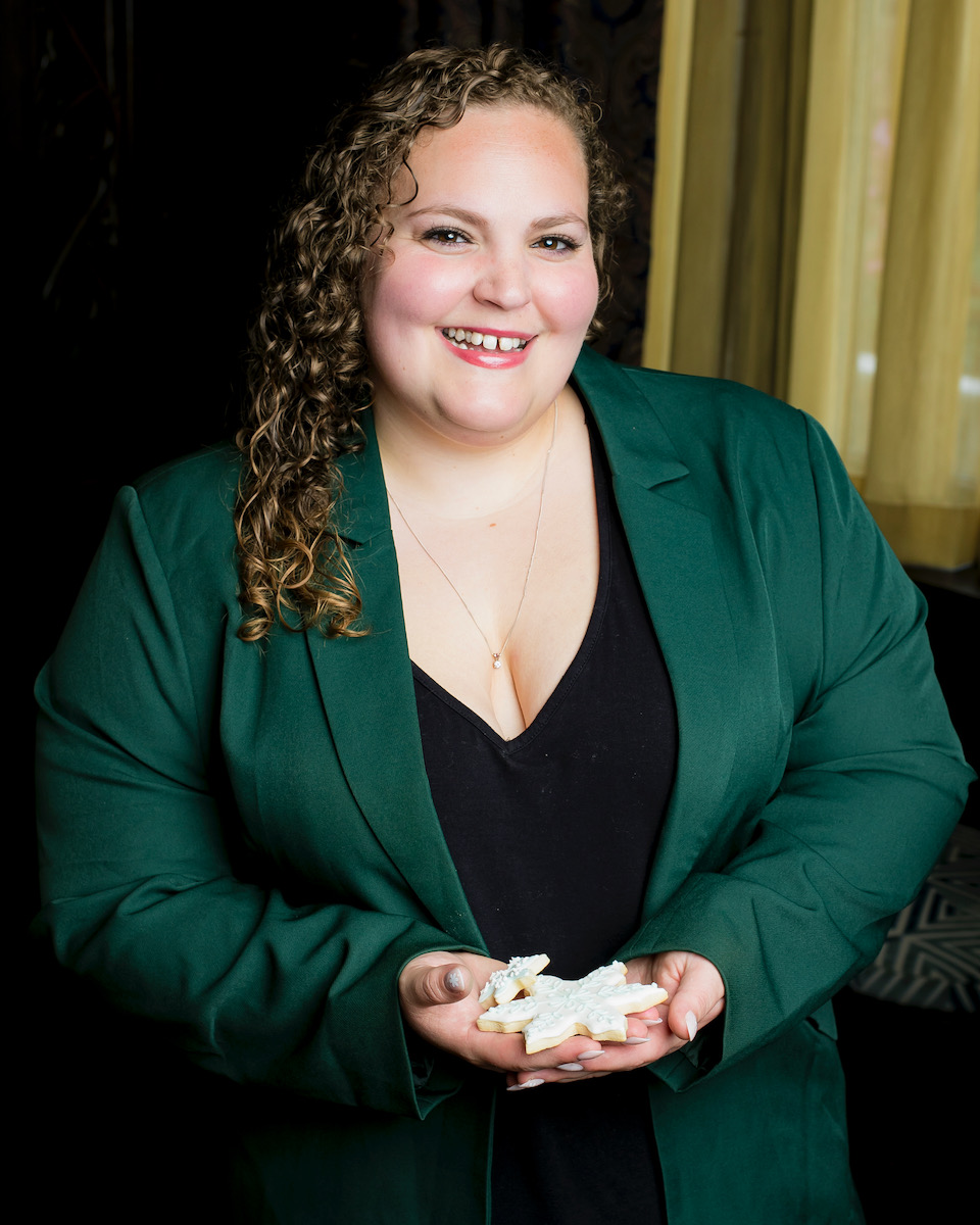 Lauren McLane, a woman in a green camisole and black shirt, holds her sugar cookies