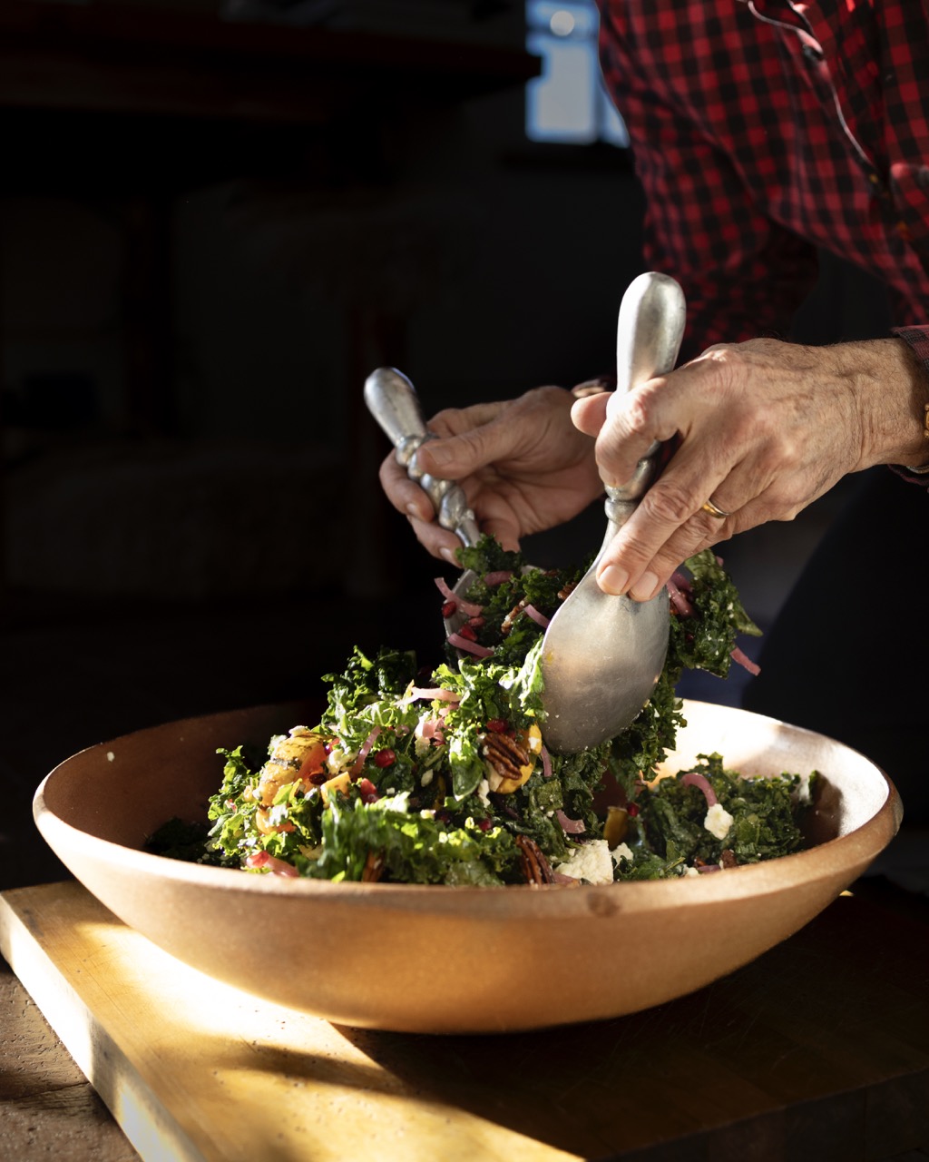 A person mixes a salad of persimmons and arugula in a big brown bowl. 