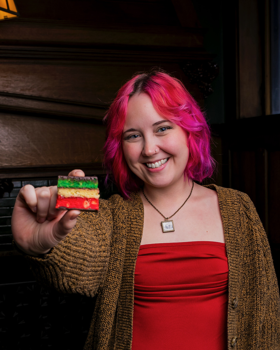 Rachel Walton, a woman with pink hair wearing a brown cardigan, holds her Italian Rainbow cookies