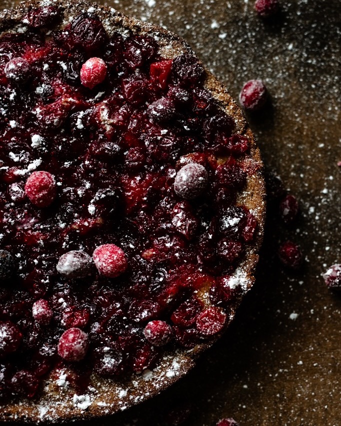 Half a cranberry cake with cranberries and powdered sugar on top.