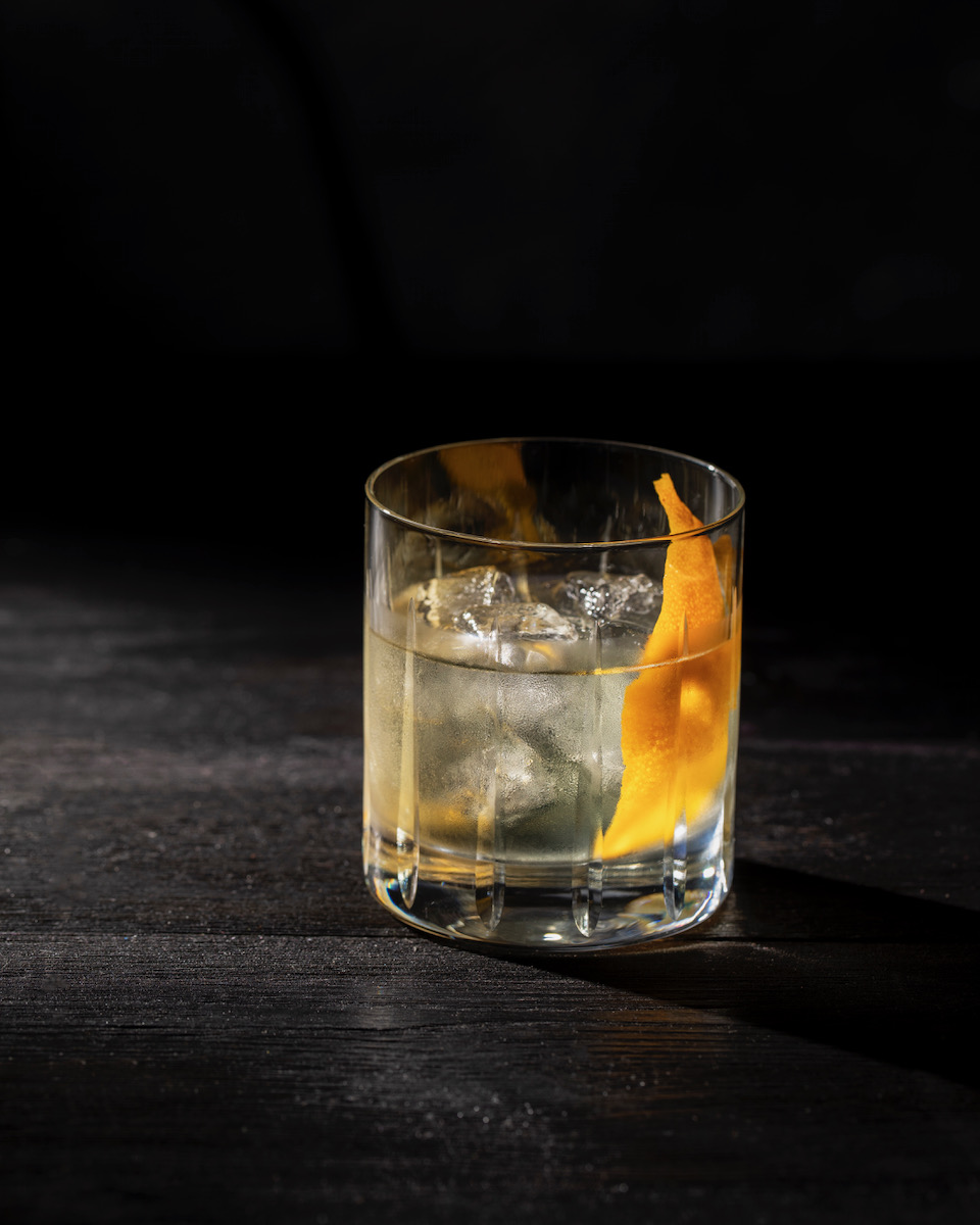 A whiskey sour cocktail with an orange peel in it on a black background