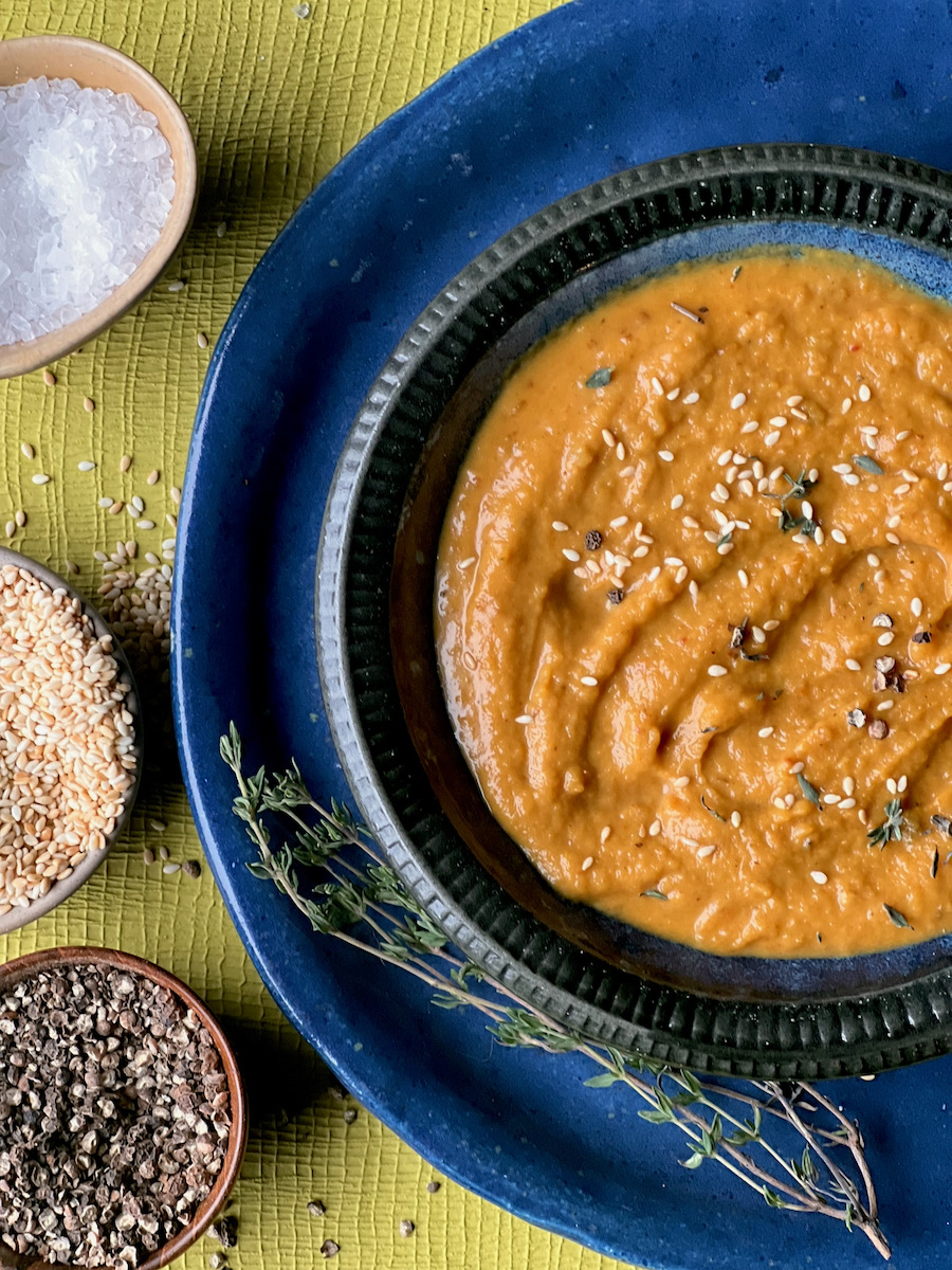 A bowl of pumpkin soup garnished with sesame seeds on a dark blue ceramic plate