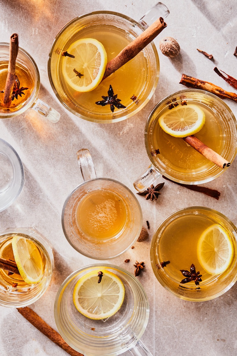 A set of hot toddy cocktails on a white tablecloth background, garnished with cinnamon