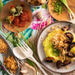 Flat-lay image of a mushroom dish served over rice and surrounded by colorful condiments and vegetables.