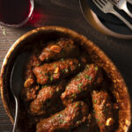 A bowl filled with braciole, featuring meat and sauce, elegantly presented on a dining table.