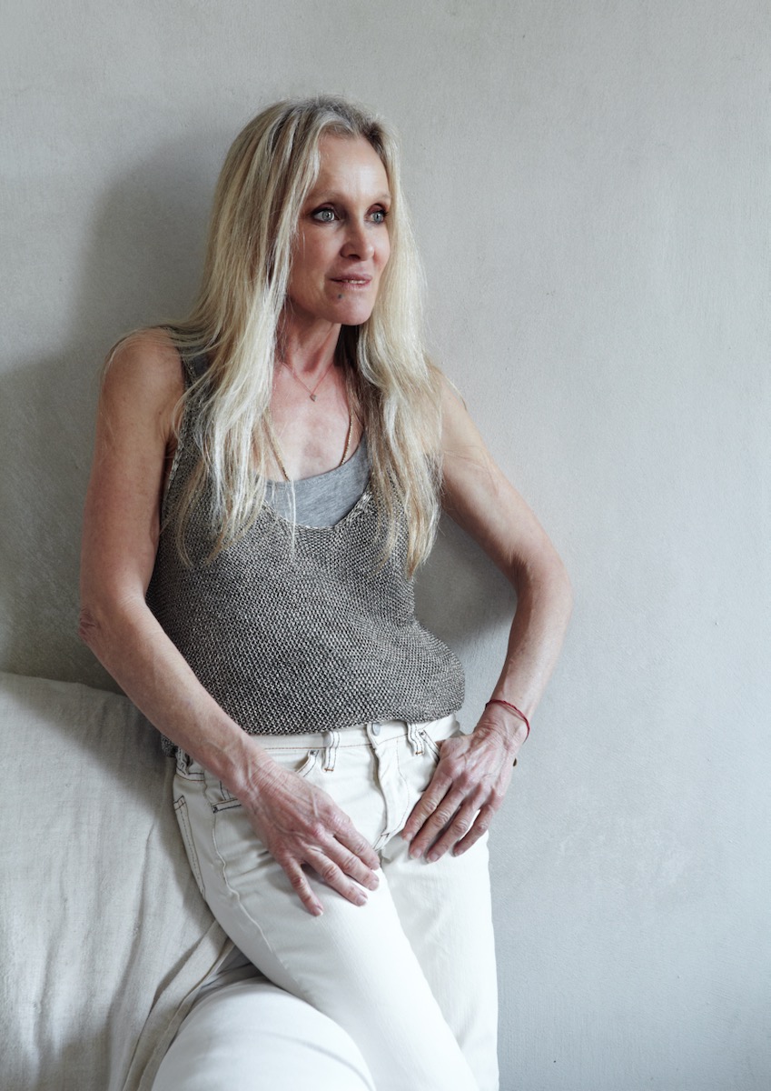 Algria Ferreira-Watling, a blonde woman dressed in white, leans against a wall