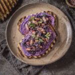 A plate of bright purple hummus topped with sesame seeds, spread on top of crostini