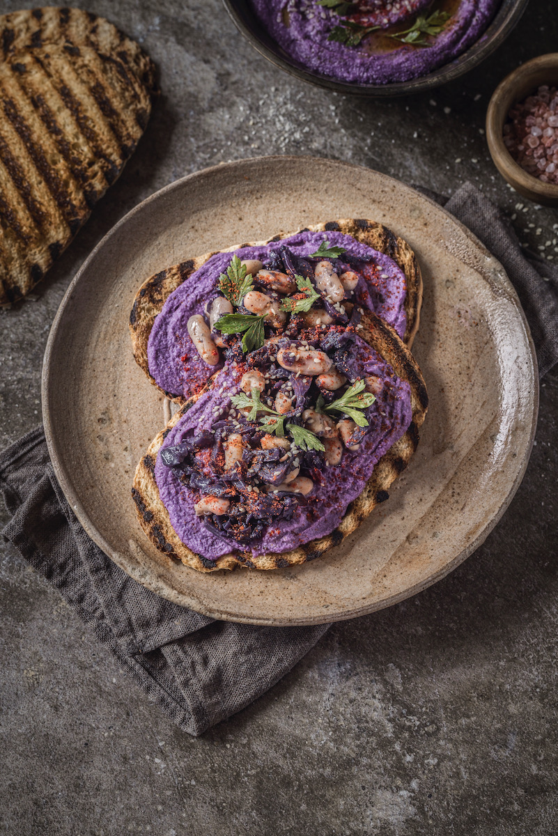 A plate of bright purple hummus topped with sesame seeds, spread on top of crostini