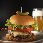 A delicious Hawaiian burger topped with bacon, pineapple, and red onion, served alongside a refreshing beer on a plate.