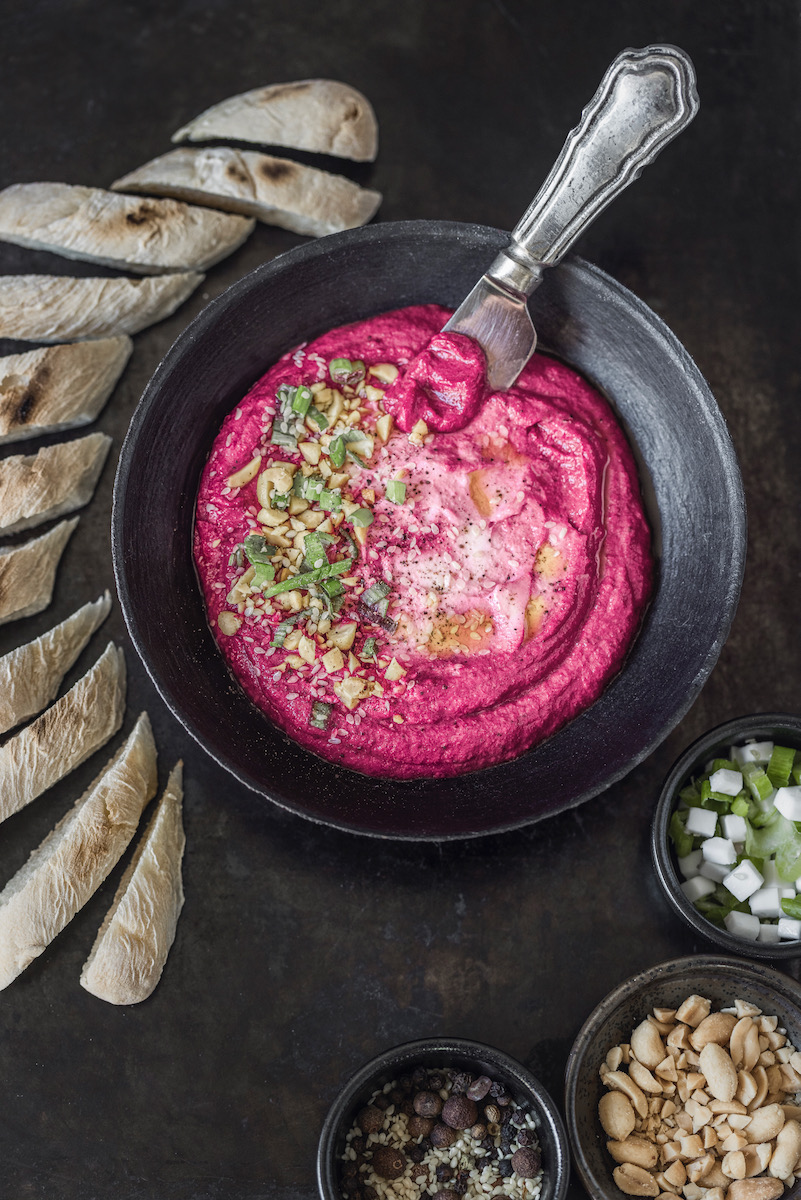 A pink bowl of beet and yogurt mousse with garnish on top of it