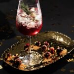 A rosemary cocktail in a white wine glass, gleaming with bright red cranberry juice and staged on a black background