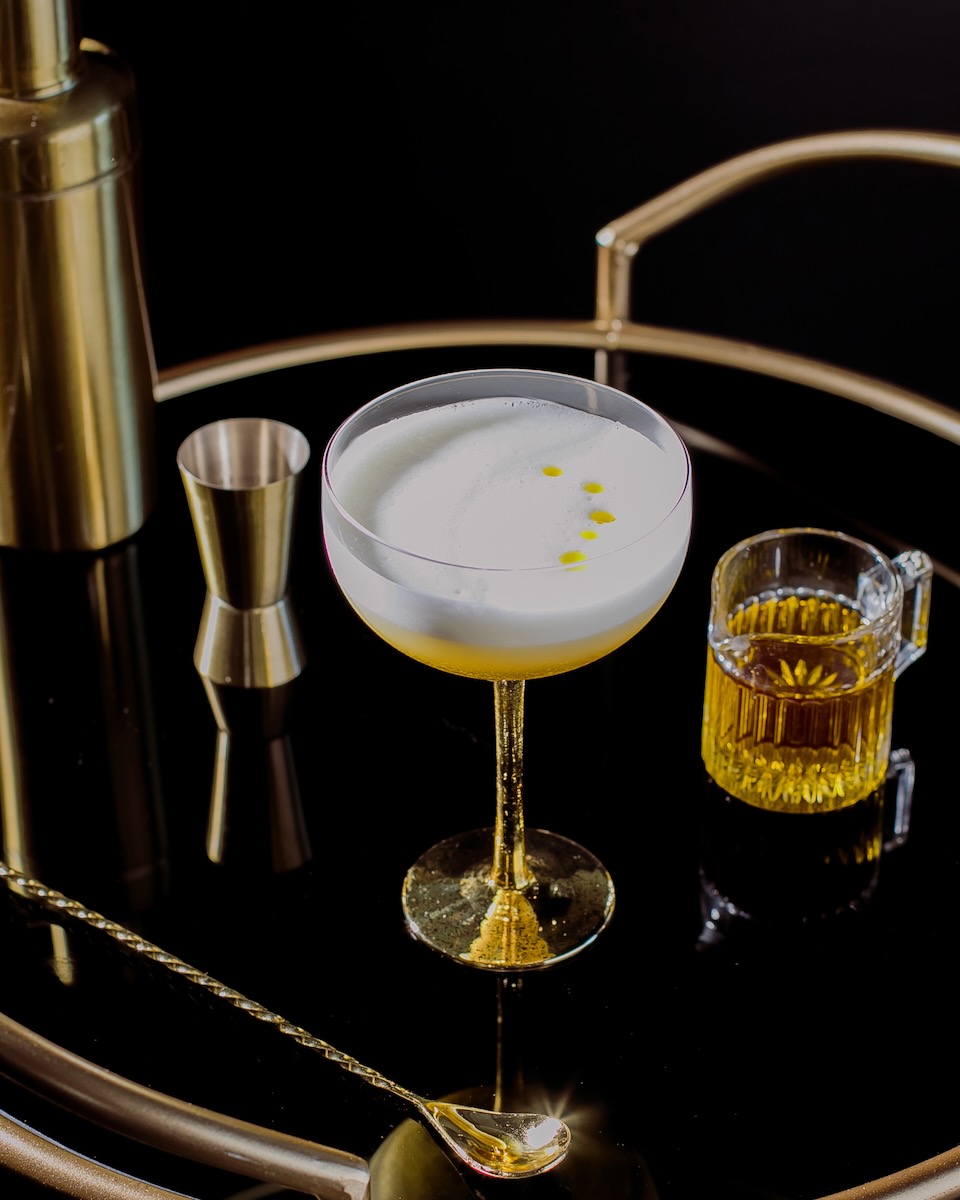 A limoncello cocktail with four drops of olive oil in it on a black background