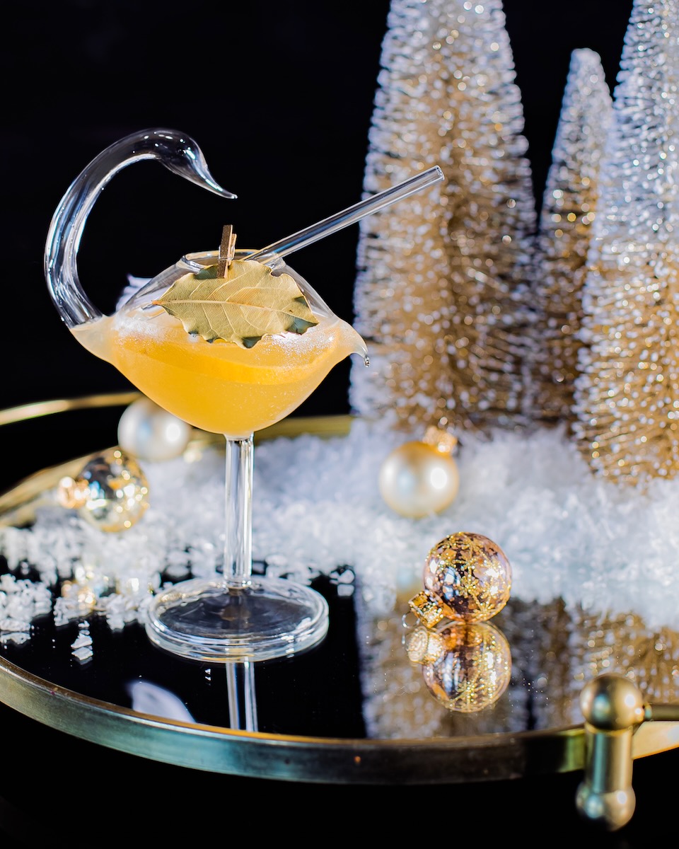 A Hemingway daiqiuri in a glass shaped like a swan, staged next to Christmas trees