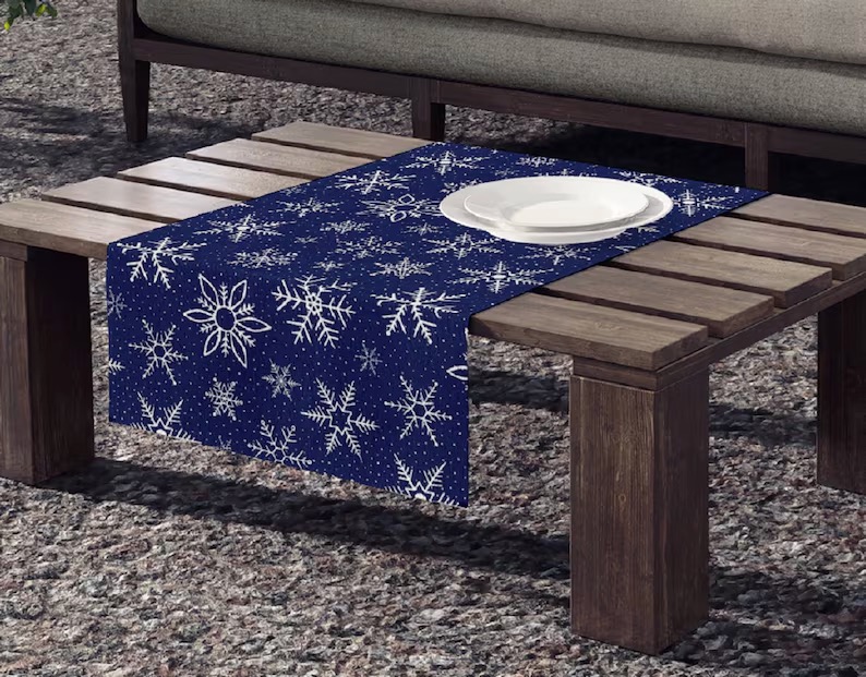 A snowflake tablecloth on a coffee table with white plates on it