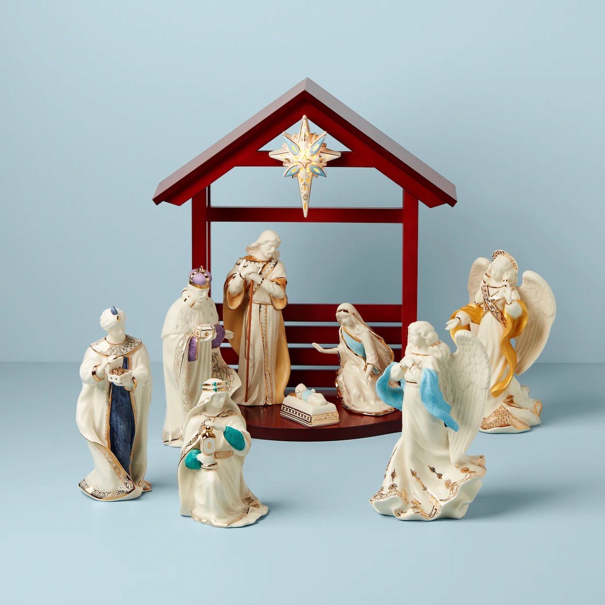 A scene of white nativity figures on a light blue background with a red créche 