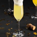 A champagne flute on a black background, topped off with coconut flakes and surrounded by festive decor