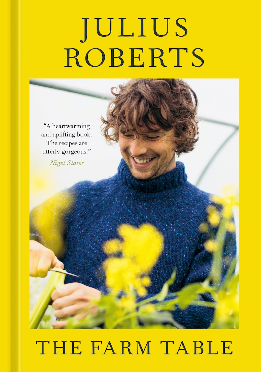 A yellow cookbook by Julius Roberts, featuring Robert smiling down at a culinary creation surrounded by yellow flowers