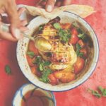 A bowl of grilled halloumi with apricots on a red background