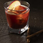 A rustic non-alcoholic old-fashioned cocktail served in a rocks glass, garnished with fresh apple slices, a cherry, and featuring a dense, foamy head.