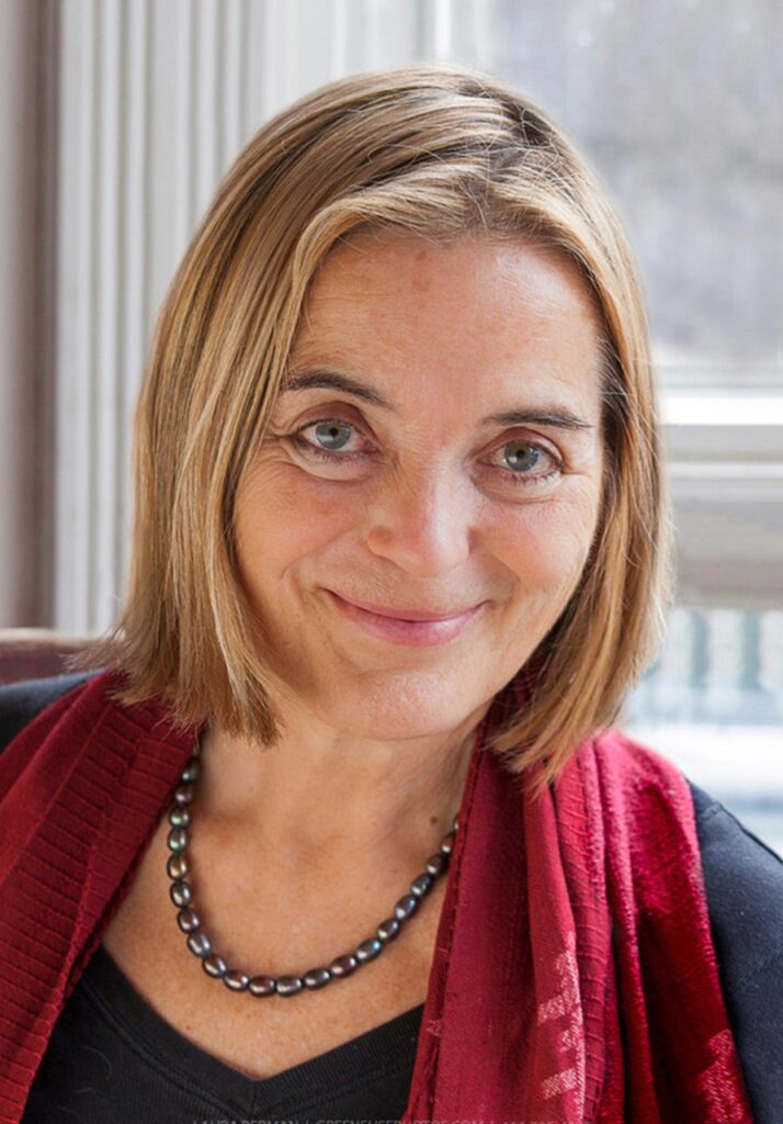 A woman author who writes about salt sits with blonde hair and a red vest and necklace as she looks up at the camera.