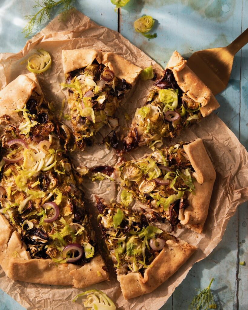 A Brussels sprout galette with red onion on it, cut into triangular slices.