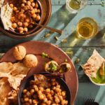 A large brown plate holds a variety of holi food including Chana Masala in two separate bowls.