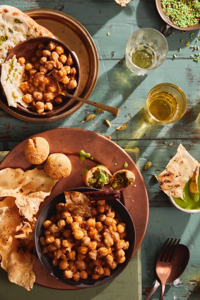 A large brown plate holds a variety of holi food including Chana Masala in two separate bowls.